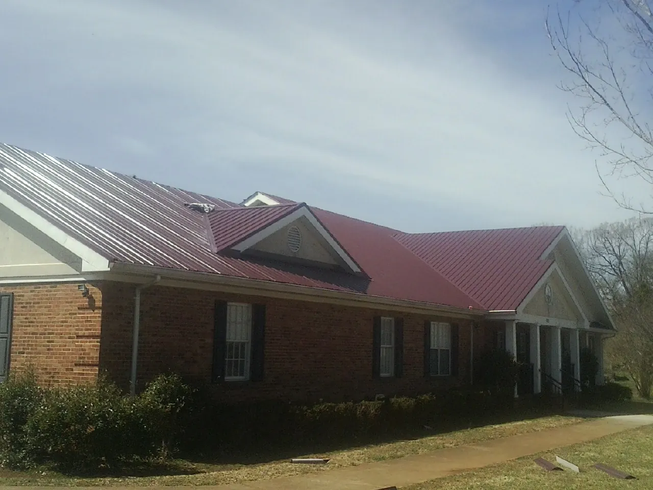 Red metal roof with gabled entries on a long brick building, from a Hail Damage Roof Repair job in Ripley