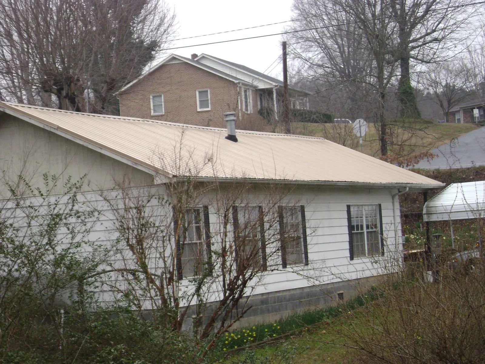 Tan metal roof on a white sided house set into a hillside — Commercial Roofing by Roofing Brothers in Ripley